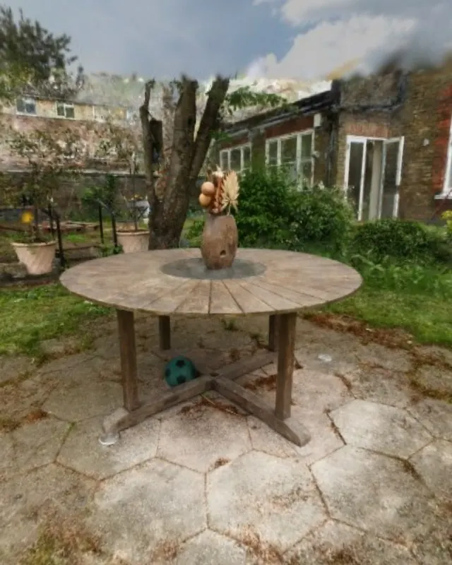 A round wooden table with a vase in a walled garden